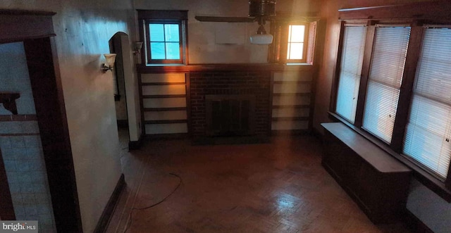 living area with arched walkways, a brick fireplace, and plenty of natural light