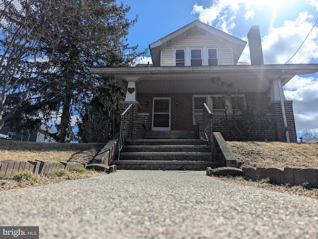 view of front of property featuring a porch, a chimney, and brick siding