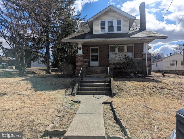 bungalow with covered porch, brick siding, and a chimney