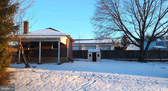 snow covered back of property with an outbuilding, brick siding, a chimney, a porch, and fence