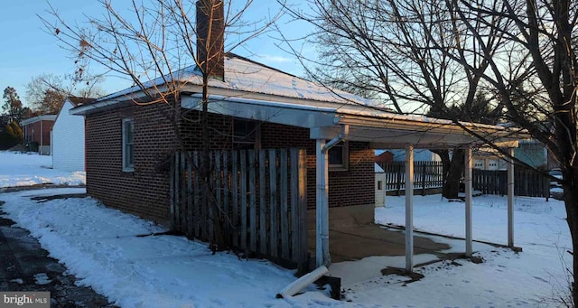 view of snow covered exterior featuring a carport, brick siding, and fence