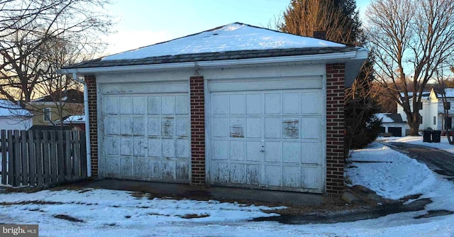 snow covered garage with a garage and fence