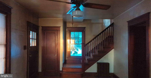 foyer entrance featuring a ceiling fan, radiator, and stairway