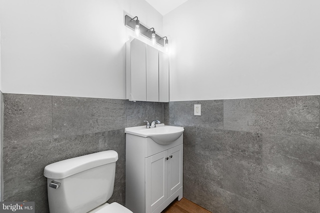 bathroom with toilet, a wainscoted wall, tile walls, and vanity