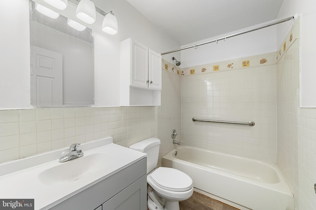 bathroom with toilet, wood finished floors, bathing tub / shower combination, vanity, and tile walls