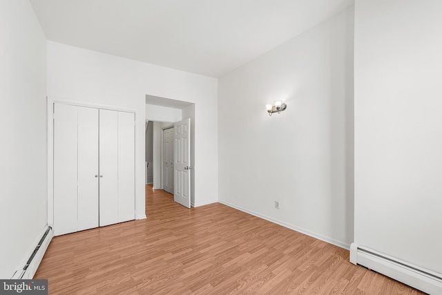 unfurnished bedroom featuring light wood finished floors, baseboards, a baseboard heating unit, and a closet