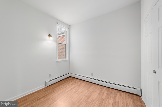 spare room with a baseboard heating unit, light wood-type flooring, and baseboards