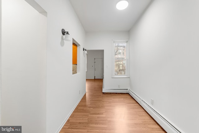 corridor featuring light wood finished floors, a baseboard radiator, and baseboards