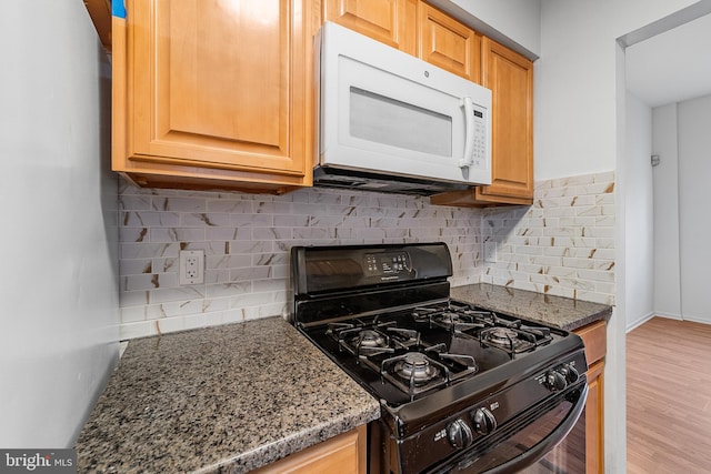 kitchen with white microwave, stone countertops, wood finished floors, decorative backsplash, and gas stove