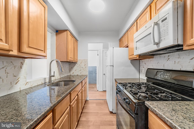 kitchen featuring white microwave, a sink, light wood finished floors, dark stone countertops, and black gas range oven