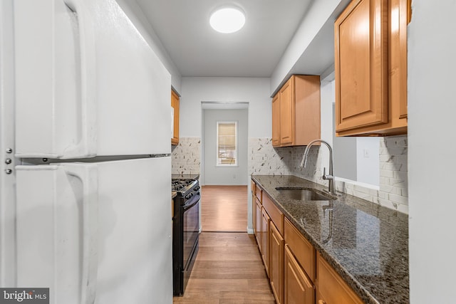 kitchen with black gas range, light wood-style flooring, a sink, freestanding refrigerator, and dark stone counters