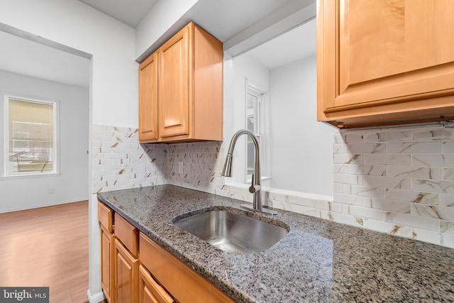 kitchen featuring a sink, light wood-style floors, baseboards, decorative backsplash, and dark stone counters