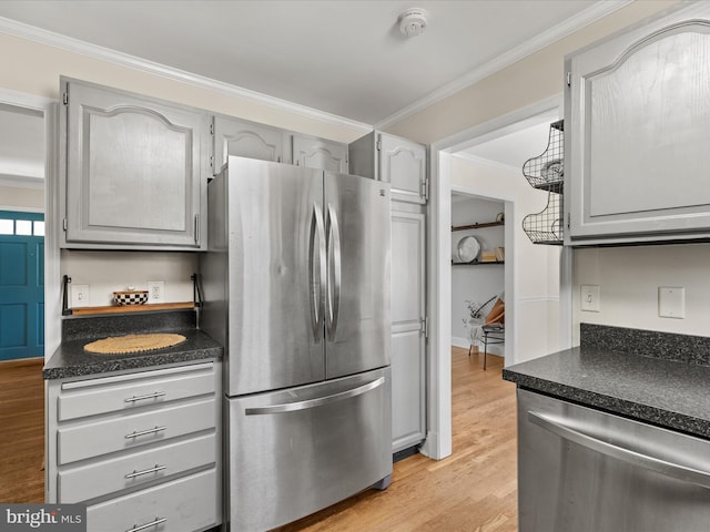 kitchen featuring dark countertops, light wood finished floors, gray cabinetry, appliances with stainless steel finishes, and crown molding