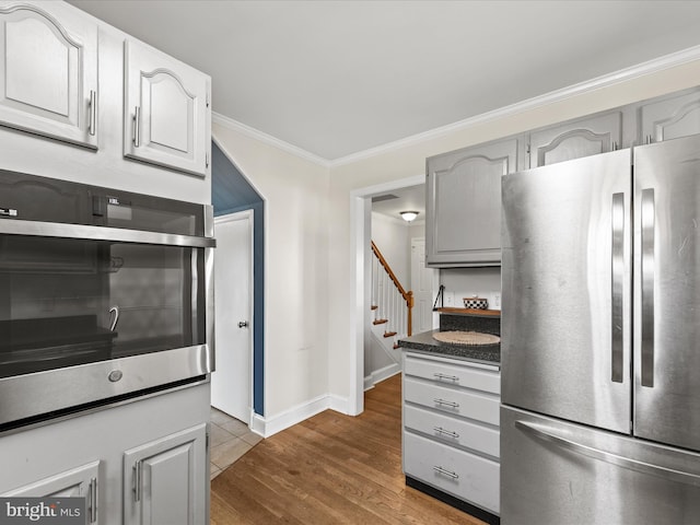 kitchen with dark countertops, gray cabinetry, stainless steel appliances, dark wood-type flooring, and crown molding