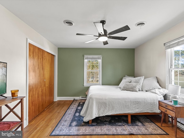 bedroom featuring a baseboard heating unit, wood finished floors, visible vents, and a closet