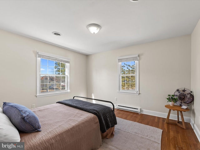 bedroom featuring a baseboard heating unit, multiple windows, wood finished floors, and visible vents