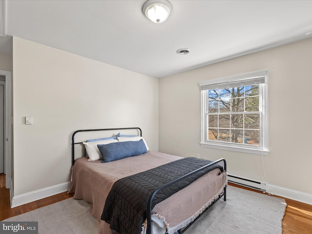 bedroom featuring baseboard heating, baseboards, visible vents, and wood finished floors