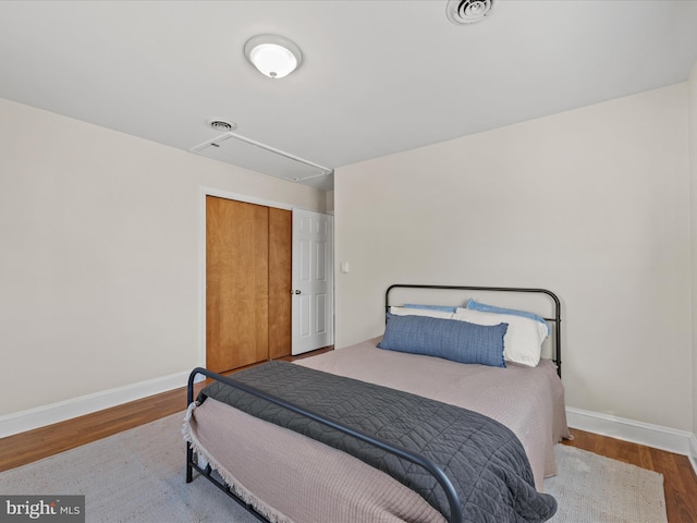 bedroom featuring wood finished floors, visible vents, baseboards, attic access, and a closet