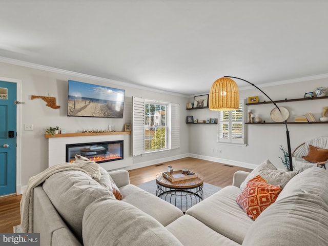 living room with a glass covered fireplace, ornamental molding, baseboards, and wood finished floors