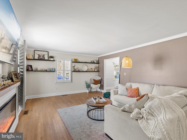 living room featuring baseboards, visible vents, ornamental molding, a glass covered fireplace, and light wood-type flooring