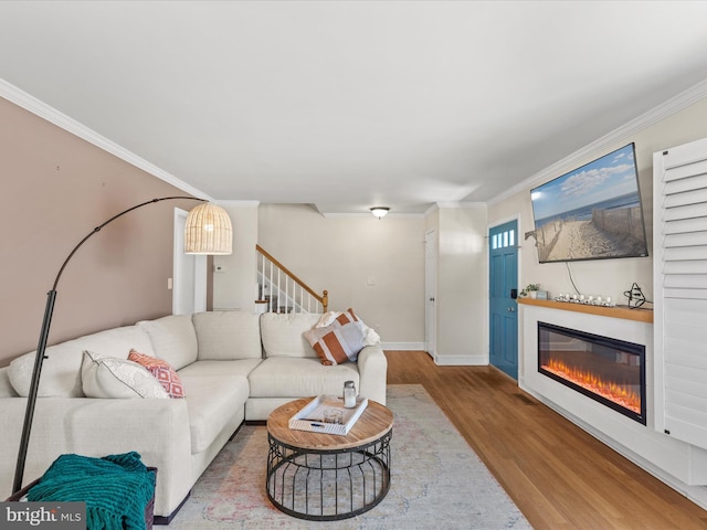 living area featuring stairway, wood finished floors, baseboards, ornamental molding, and a glass covered fireplace