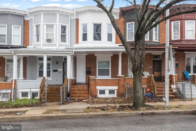 townhome / multi-family property with a porch, cooling unit, and brick siding