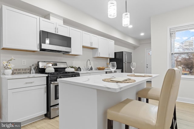 kitchen featuring light wood finished floors, white cabinets, a center island, stainless steel appliances, and a kitchen bar