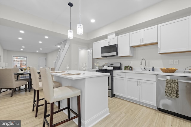 kitchen with a center island, light wood finished floors, appliances with stainless steel finishes, a sink, and a kitchen bar