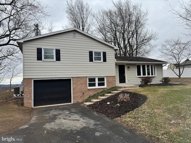 tri-level home with a garage, central AC unit, brick siding, and driveway