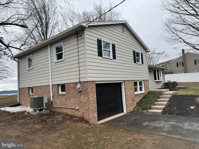 view of property exterior with driveway, fence, cooling unit, a garage, and brick siding