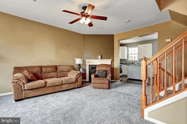 carpeted living room with stairs, a ceiling fan, and a glass covered fireplace