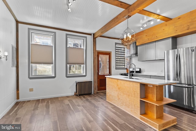 kitchen featuring wood finished floors, light countertops, wall chimney range hood, freestanding refrigerator, and radiator heating unit