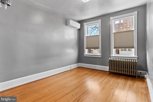 unfurnished room featuring a wall unit AC, radiator heating unit, baseboards, and hardwood / wood-style floors