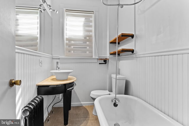 bathroom featuring wainscoting, toilet, radiator heating unit, a freestanding tub, and a sink