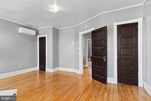 empty room featuring crown molding, light wood finished floors, a wall mounted AC, and baseboards