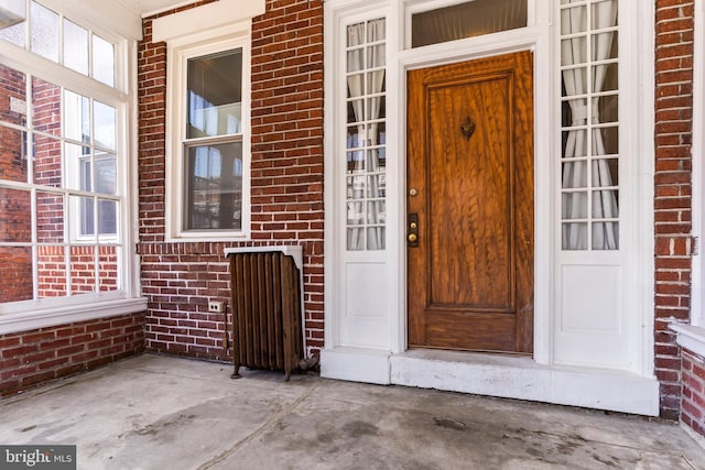 doorway to property featuring a porch and brick siding