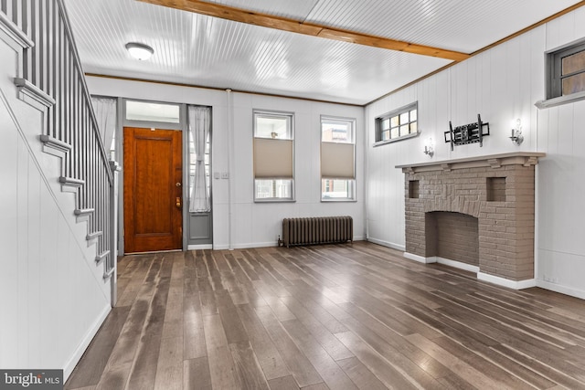 foyer featuring baseboards, radiator, stairway, hardwood / wood-style floors, and a brick fireplace