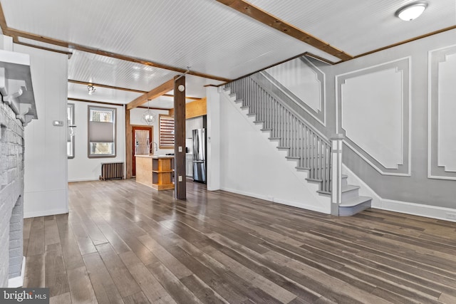 unfurnished living room with baseboards, dark wood finished floors, radiator, beamed ceiling, and stairs