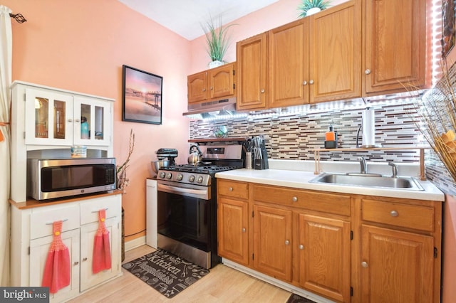 kitchen featuring under cabinet range hood, a sink, light countertops, appliances with stainless steel finishes, and tasteful backsplash