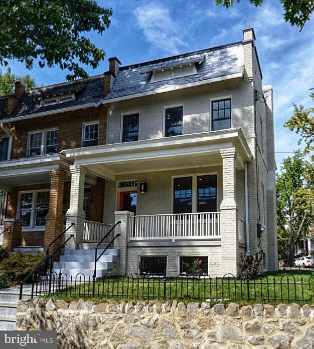 view of front of house with a porch, mansard roof, brick siding, and a fenced front yard