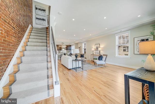 unfurnished living room with recessed lighting, brick wall, stairs, and light wood-type flooring