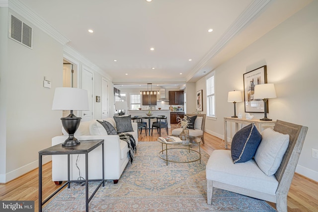 living room with crown molding, light wood-style floors, visible vents, and baseboards