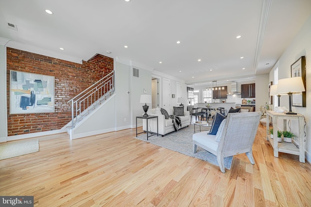 living area with stairway, visible vents, brick wall, ornamental molding, and light wood-type flooring