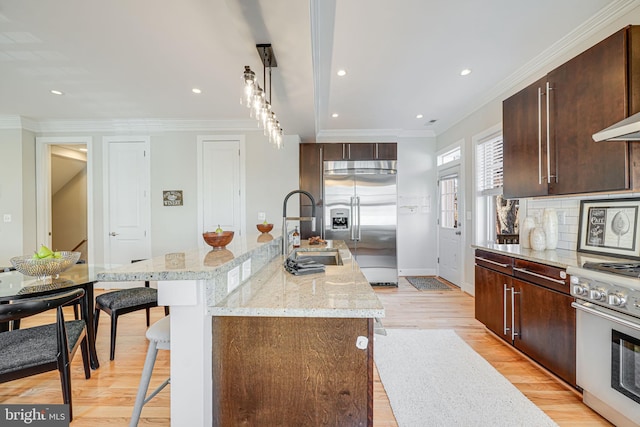 kitchen with a sink, a kitchen breakfast bar, light wood-style floors, appliances with stainless steel finishes, and decorative backsplash