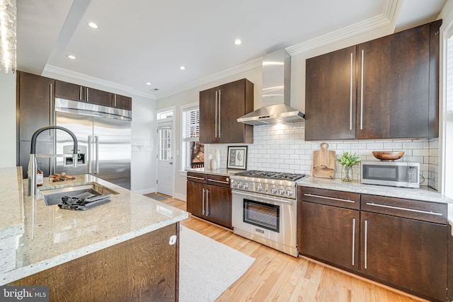 kitchen featuring crown molding, wall chimney range hood, dark brown cabinetry, light wood-type flooring, and premium appliances