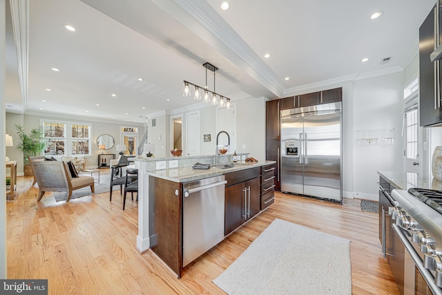 kitchen with a center island with sink, light wood-type flooring, ornamental molding, high end appliances, and a sink