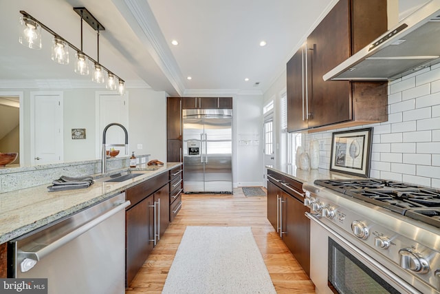 kitchen with light wood finished floors, a sink, ornamental molding, stainless steel appliances, and exhaust hood