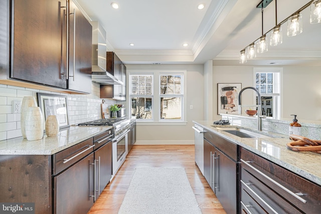 kitchen featuring light wood finished floors, stainless steel appliances, a sink, dark brown cabinets, and wall chimney exhaust hood