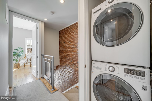 washroom featuring laundry area, brick wall, stacked washing maching and dryer, and light wood-type flooring