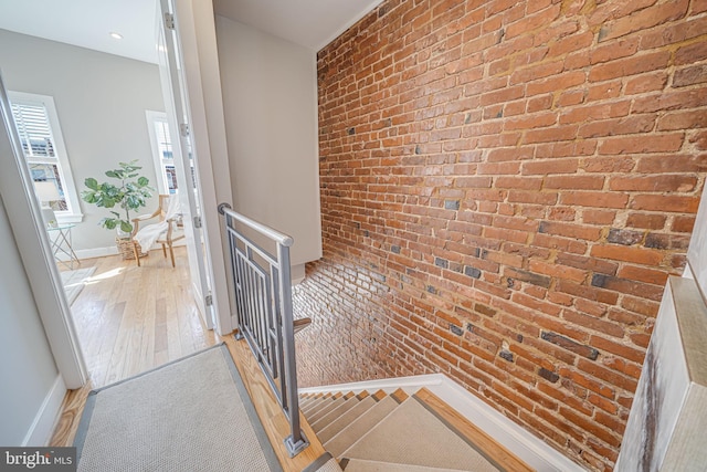 stairs with wood finished floors, baseboards, and brick wall